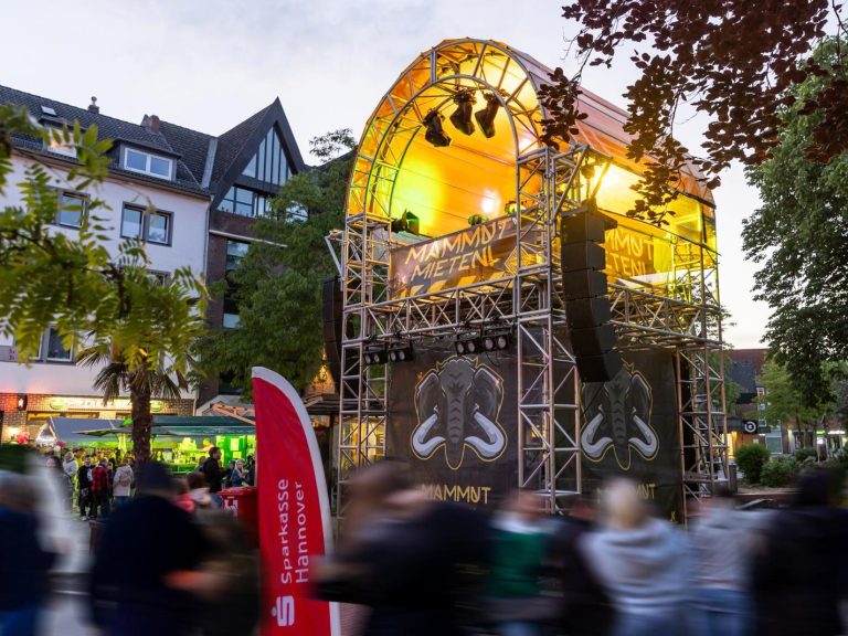 Bühne mit Lichtern, umgeben von Zuschauern auf einem festlichen Platz.
